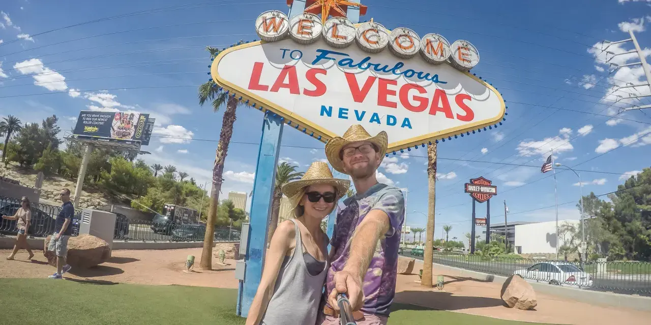 Para co przywieźć ze Stanów? Pamiątkę z Las Vegas! Uśmiechnięta para pozuje do selfie pod słynnym znakiem.