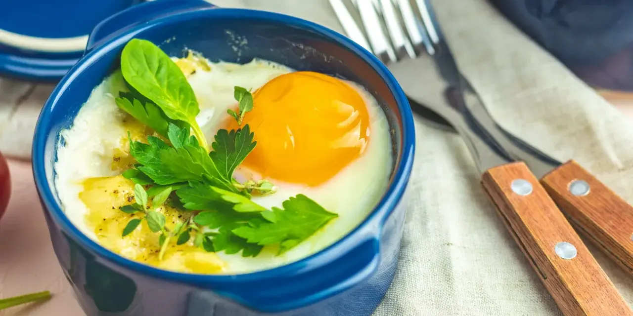 Un œuf cocotte appétissant dans un ramequin bleu, garni d'herbes fraîches. Un délice pour le petit-déjeuner.
