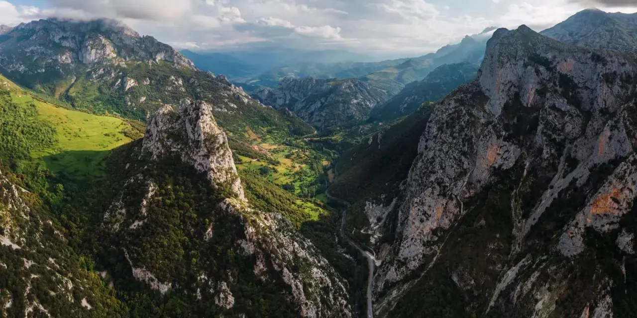 Majestätische Berge der Picos de Europa, grüne Täler und eine Straße, die sich durch die zerklüftete Landschaft schlängelt.