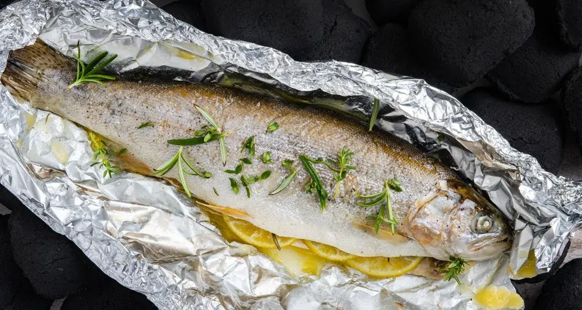 Eine ganze Forelle vom Grill in Alufolie, mit Zitronenscheiben und Rosmarin verfeinert, bereit für den Genuss.