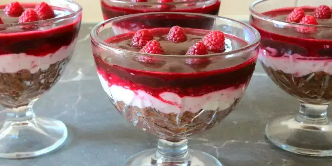 Pyszny deser z mascarpone i galaretką malinową w pucharkach, ozdobiony świeżymi malinami.