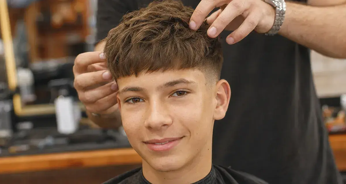 Ein Junge mit einem modernen Haarschnitt, der von einem Friseur gestylt wird. Diese Frisuren für Jungs sind im Trend.
