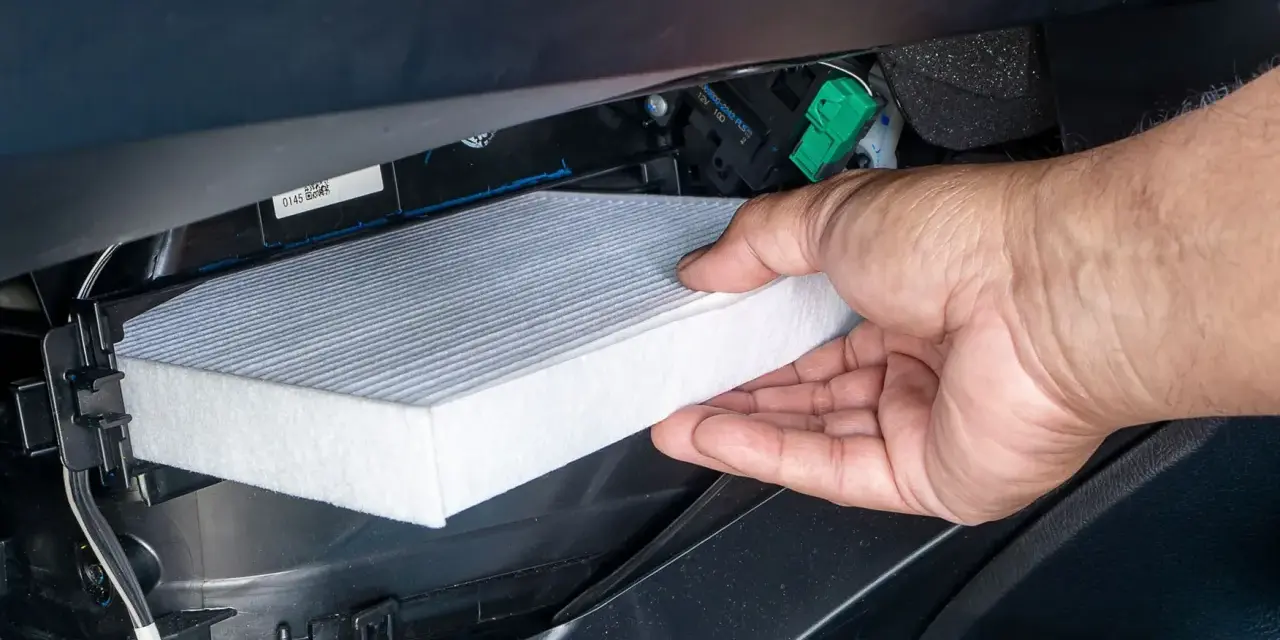 A hand removes a new cabin air filter from its packaging, ready to install it. This shows how to change cabin air filter for cleaner air.
