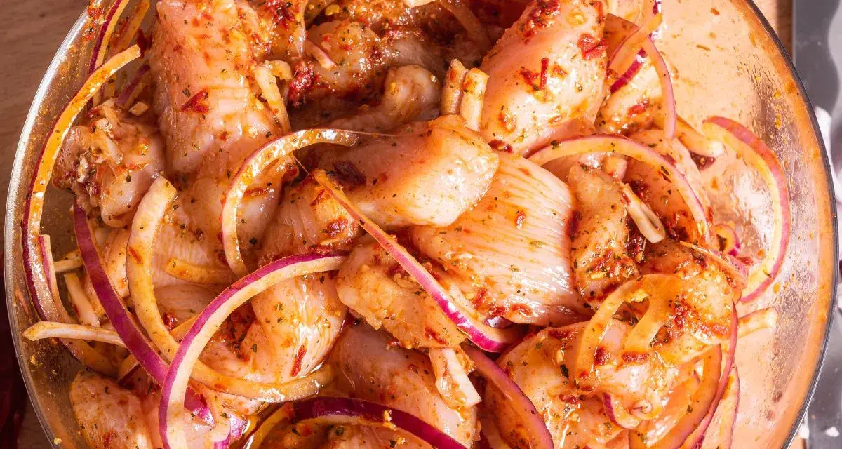Kawałki kurczaka w misce z czerwoną cebulą i przyprawami, gotowe na grill. Pyszna marynata do kurczaka na grilla.