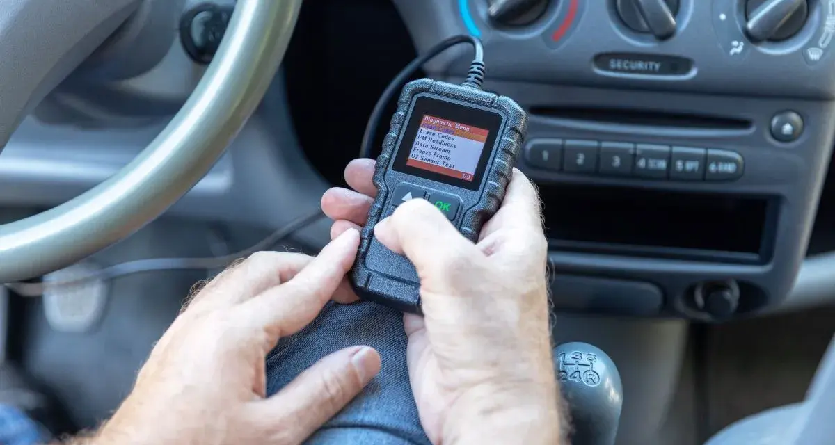 Ręce trzymające skaner diagnostyczny, który pokazuje menu z opcją "02 Sensor Test". Urządzenie może pomóc zdiagnozować problemy z czujnikiem spalania stukowego.