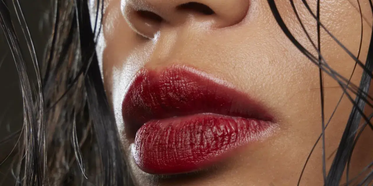 Labbra sensuali con rossetto ciliegia, un colore audace che esalta la bellezza naturale. Capelli bagnati e pelle luminosa completano il look.