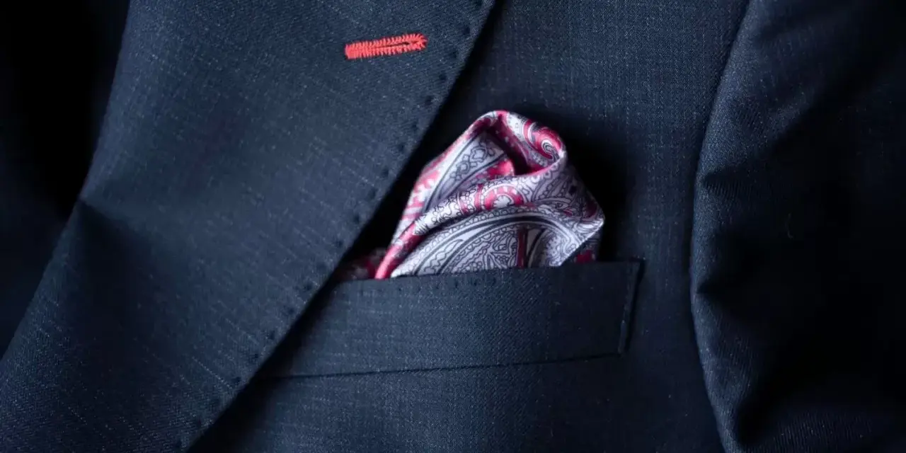 Elegancka poszetka w paisley do granatowego garnituru, z subtelnym czerwonym przeszyciem na klapie.