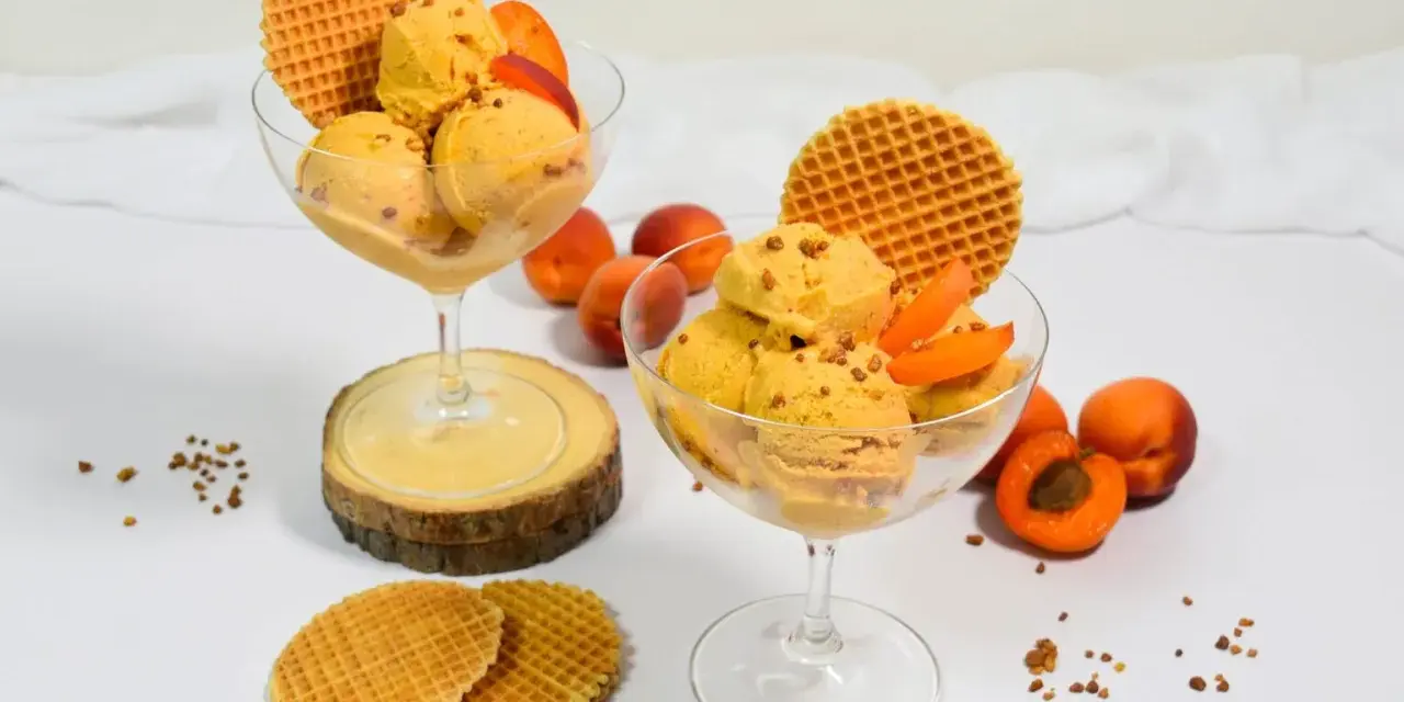 Zwei Gläser mit cremigem Aprikosen Eis, garniert mit frischen Aprikosenstücken und Waffeln. Ein sommerlicher Genuss!