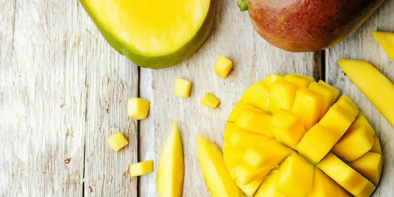 Czy pies może mango? Na drewnianym blacie leżą soczyste kawałki mango, pokrojone w kostkę i paski. Obok całe, dojrzałe owoce.