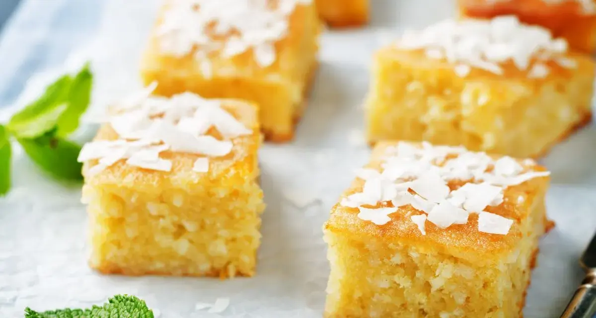 Fette di torta al cocco dorata, guarnite con scaglie di cocco e foglie di menta fresca.