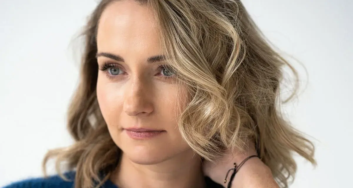 Zuzanna Irena Grabowska z burzą blond włosów i niebieskimi oczami, w granatowym swetrze.