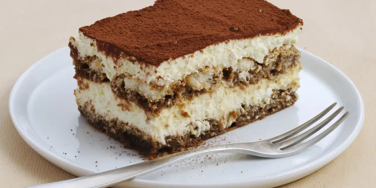 Une part de tiramisu sans oeuf, légère et aérienne, saupoudrée de cacao, sur une assiette blanche avec une fourchette.