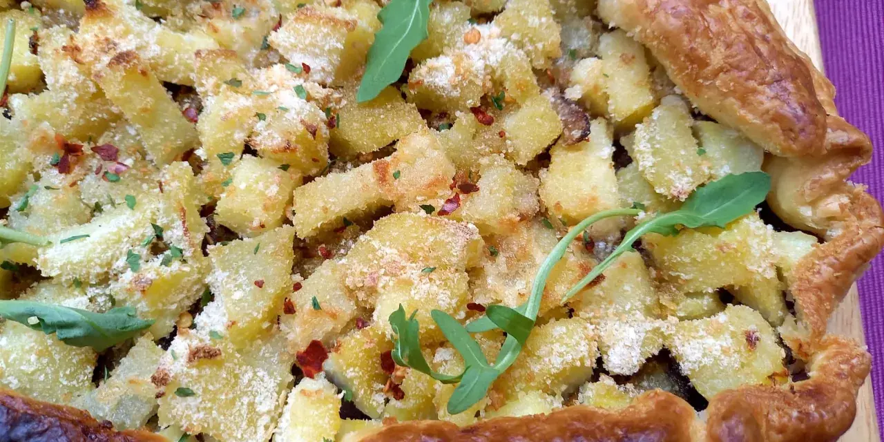 Torta salata patate e cipolle dorata e croccante, guarnita con rucola e peperoncino.