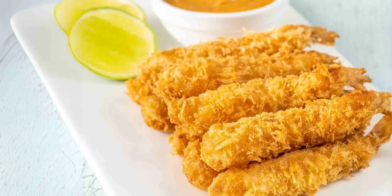 Crujientes gambas a la gabardina doradas, servidas con rodajas de lima y una salsa cremosa.