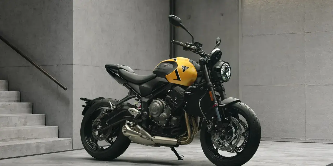 Żółty motocykl Triumph Trident 660 z czarnymi akcentami stoi na betonowej posadzce obok schodów.