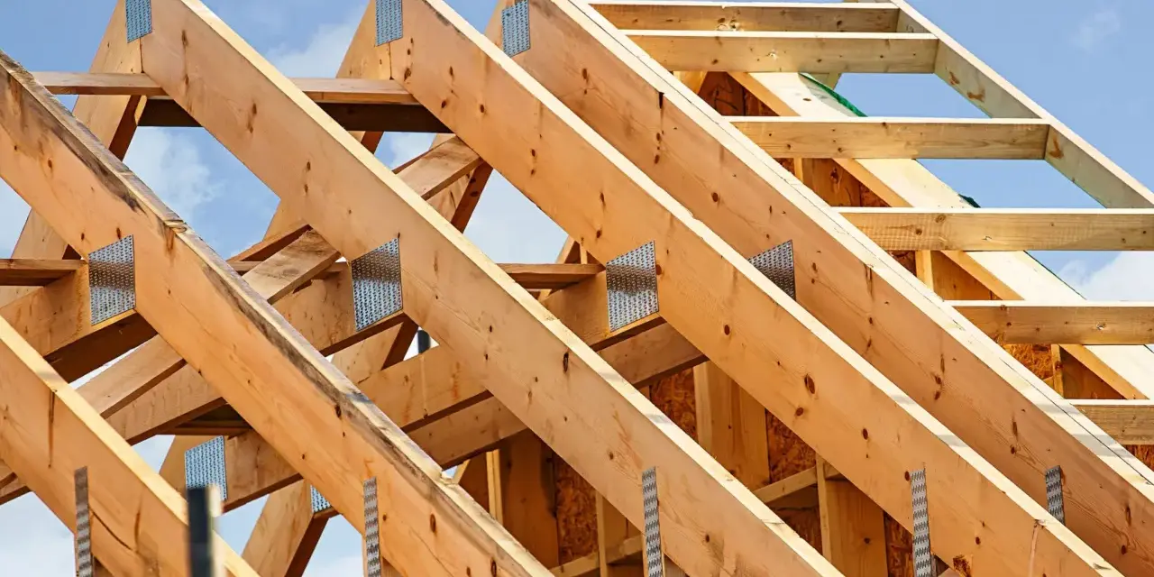 Structure en bois d'une charpente de toiture, avec des poutres assemblées par des connecteurs métalliques sous un ciel bleu.