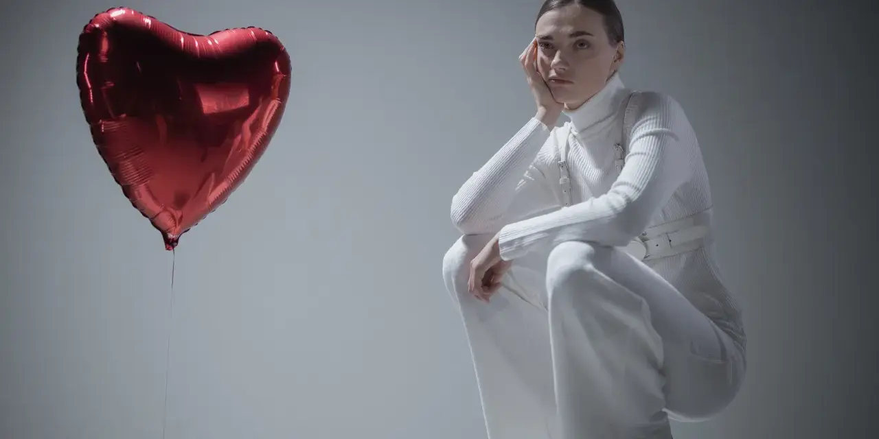 Kobieta w białym stroju siedzi przy czerwonym balonie w kształcie serca, jakby przeżywała zespół Otella.