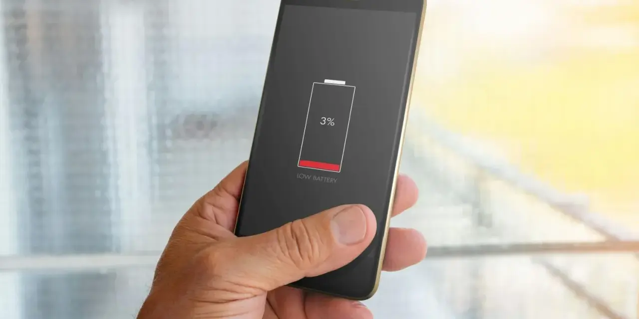 En hand håller en mobil med 3% batteri. Bakgrunden visar suddiga appaktiviteter.