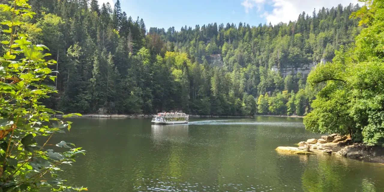 Bateau naviguant sur une rivière bordée de forêts luxuriantes, un paysage typique des chutes du Doubs.