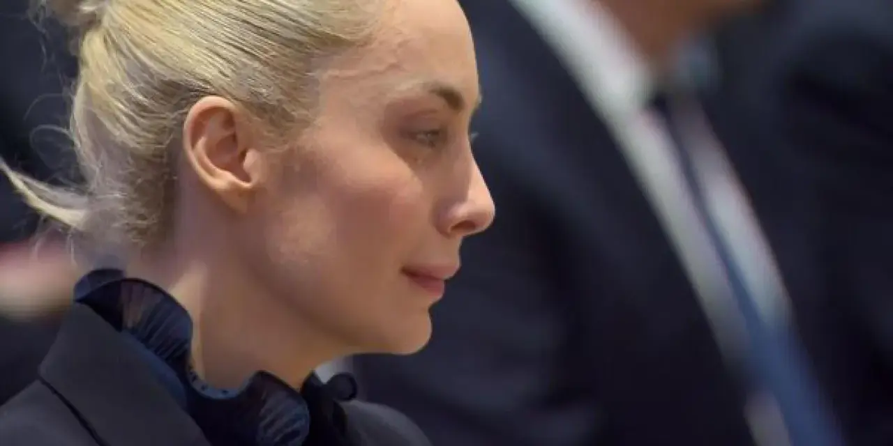 Marta Fascina, con i capelli raccolti, indossa un abito scuro. La sua espressione pensierosa suggerisce un momento di riflessione prima di un evento importante, forse legato a Silvio Berlusconi.