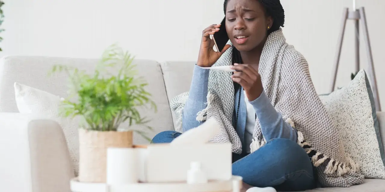 Femme malade au téléphone, thermomètre en main, elle doit se mettre en arrêt maladie avant entretien préalable licenciement.