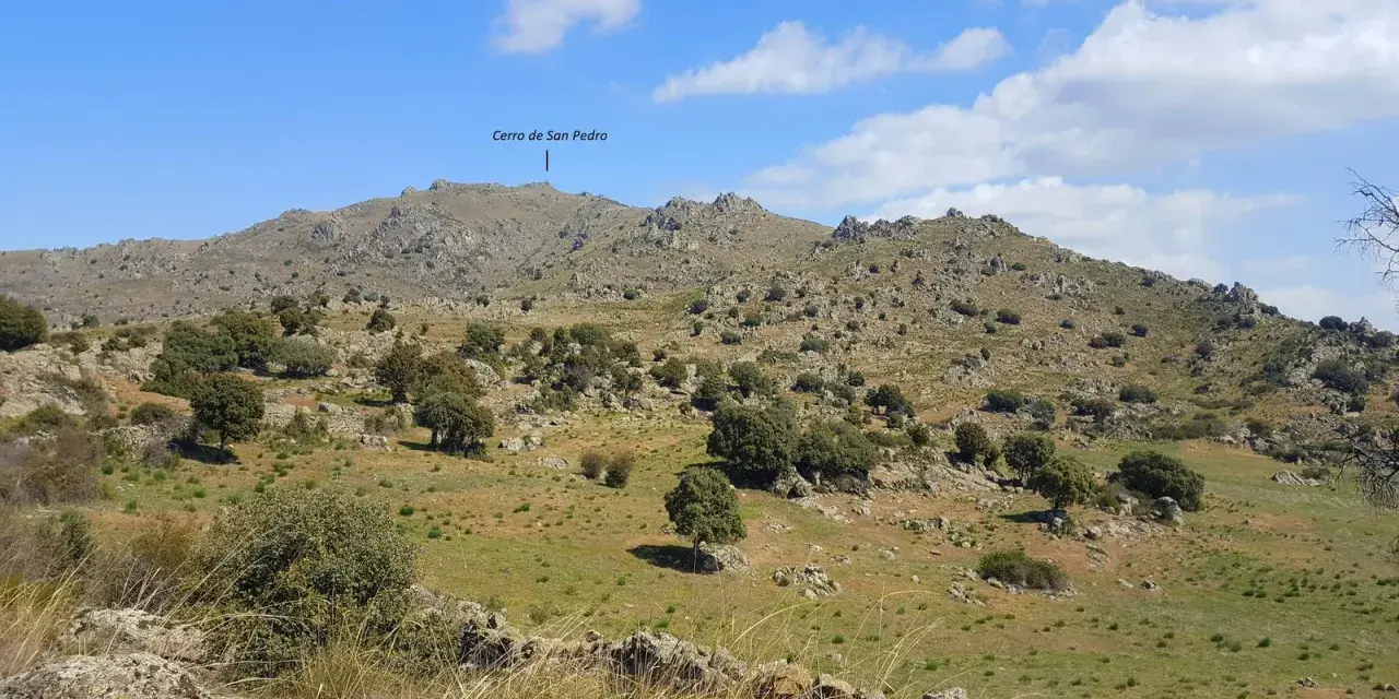 Paisaje rocoso y verde con el **cerro de San Pedro** en Colmenar Viejo al fondo.