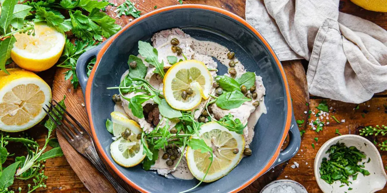 Vitello tonnato i en skål, toppad med citronskivor, kapris och ruccola. Serveras med citroner och färska örter.