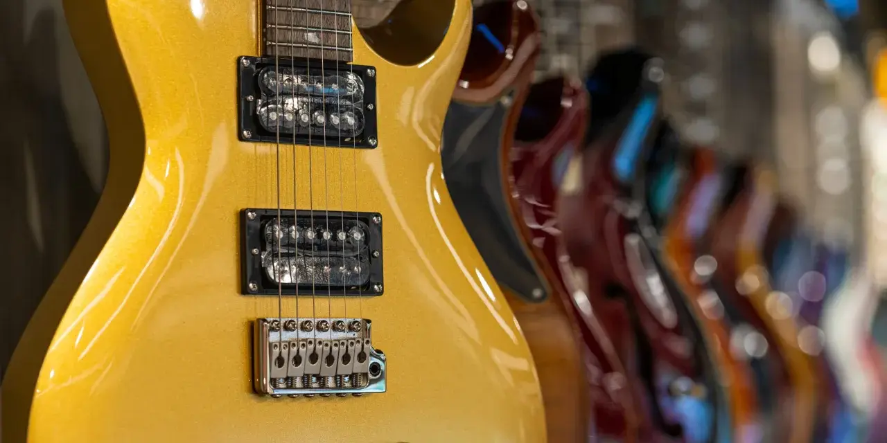 Guitarra eléctrica dorada con pastillas de **single coil** en primer plano, seguida de otras guitarras de colores.