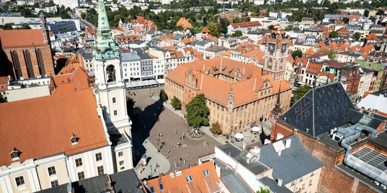 Widok na rynek i zabytkowe budynki Torunia, jednego z obiektów UNESCO w Polsce. Widać Ratusz Staromiejski i wieżę kościoła.