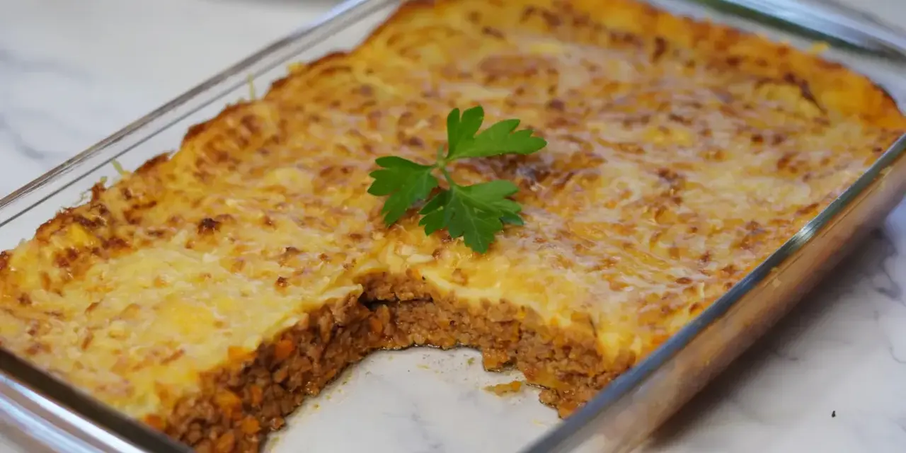 Pastel de papa recién horneado en refractario de vidrio, con una porción retirada, decorado con perejil fresco.