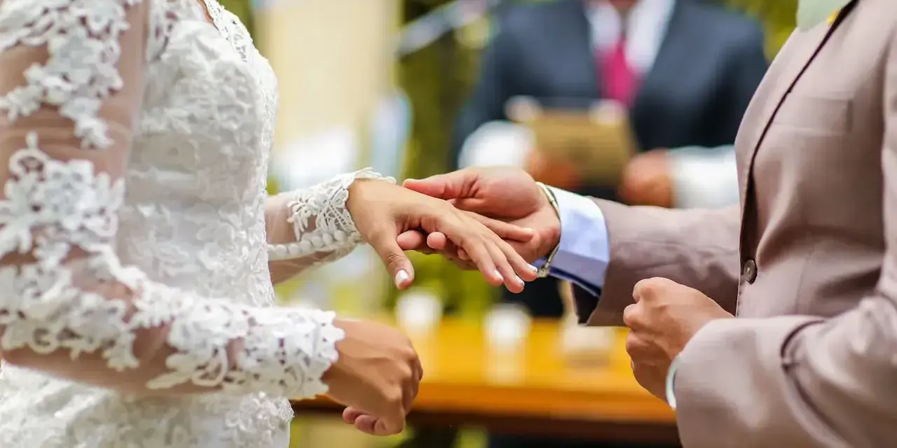 Pan młody zakłada obrączkę na palec panny młodej. W tle urzędnik udziela ślubu. Zastanawiasz się, ile kosztuje ślub cywilny?