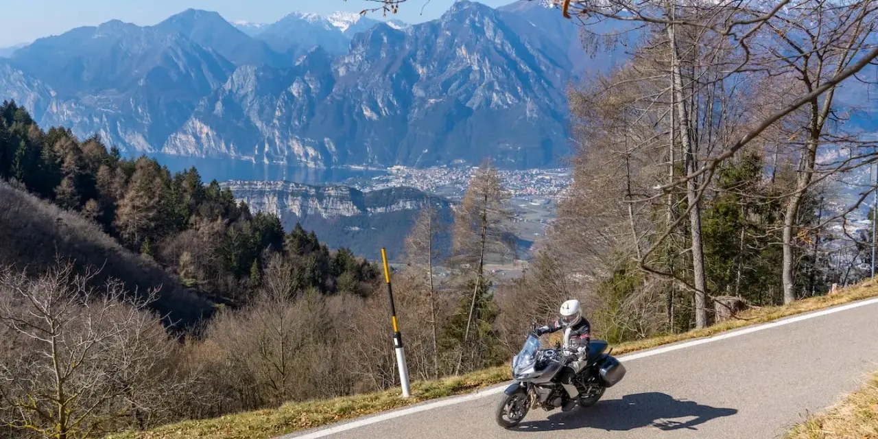 Motociclista in un panoramico motogiro Lombardia, con montagne maestose e un lago sullo sfondo.