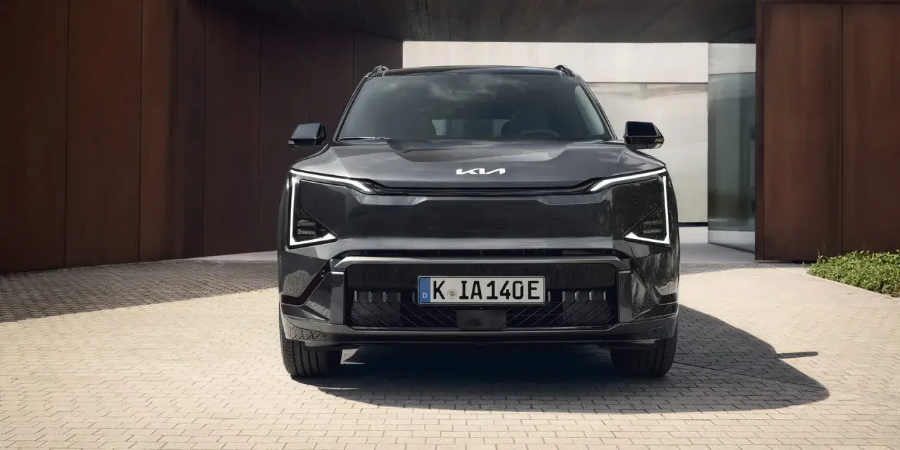 Szary SUV Kia EV5 z charakterystycznymi światłami LED, zaparkowany przed nowoczesnym budynkiem.