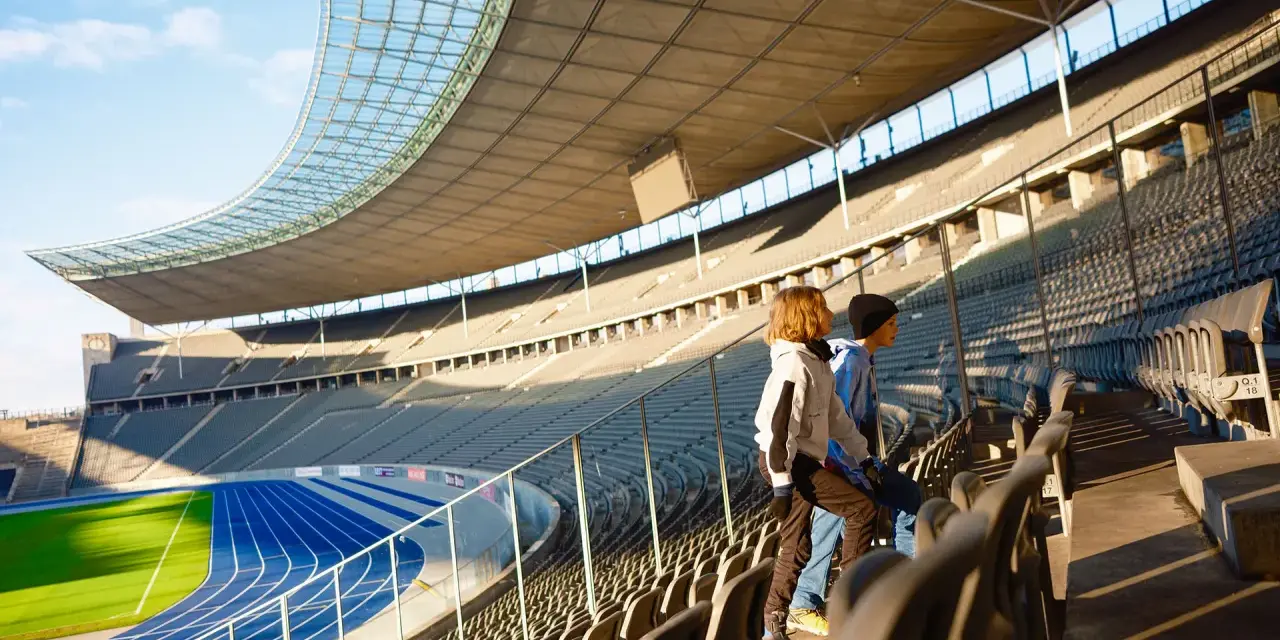 Zwei Kinder stehen auf den Rängen des Olympiastadion Berlin und blicken auf die Laufbahn.