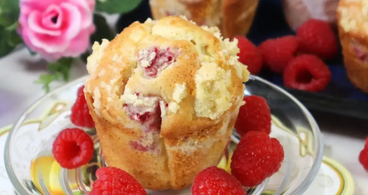 Pyszne muffinki z malinami, posypane kruszonką, otoczone świeżymi malinami.