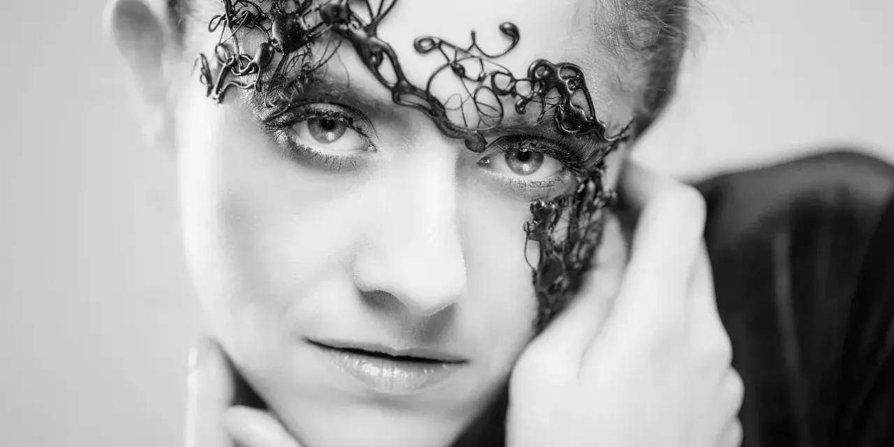 Intrygująca fotografia beauty. Kobieta z ozdobnym, czarnym makijażem na twarzy, przypominającym koronkę.