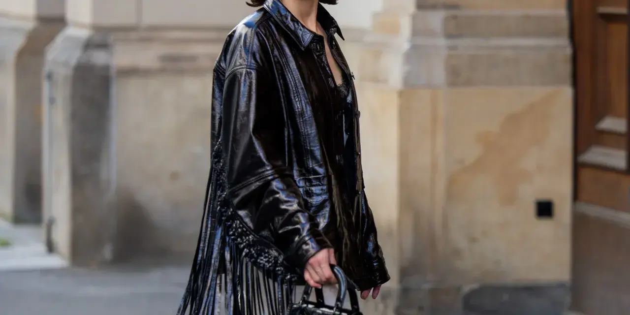Mujer con vestido negro y chaqueta de charol con flecos. Un look audaz para combinar vestido negro con chaqueta.
