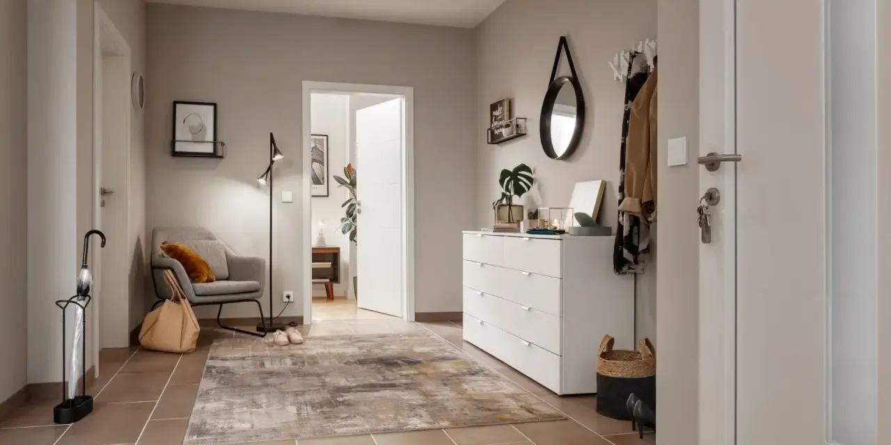 Stilvoller Flur gestalten: Grauer Sessel, Teppich, weiße Kommode mit Spiegel und Garderobe schaffen eine einladende Atmosphäre.