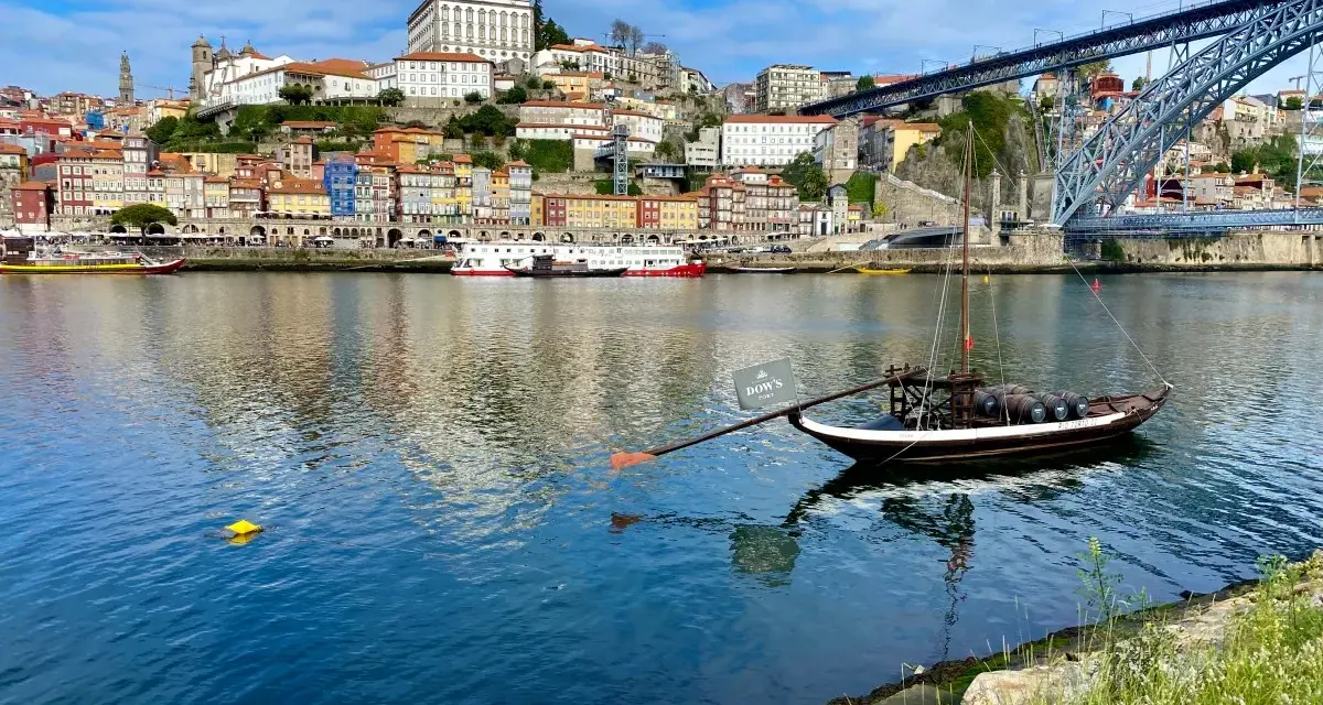 A traditional Rabelo boat with barrels, a symbol of Porto's wine heritage, floats on the Douro River. This iconic view is a must-see for any Porto travel guide.