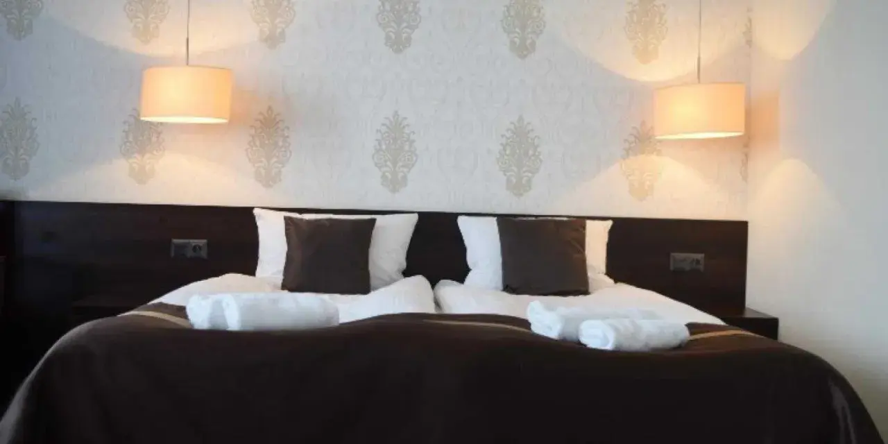 Przytulny pokój hotelowy z podwójnym łóżkiem, białymi ręcznikami i lampami. Czy można wynająć pokój w hotelu mając 17 lat?