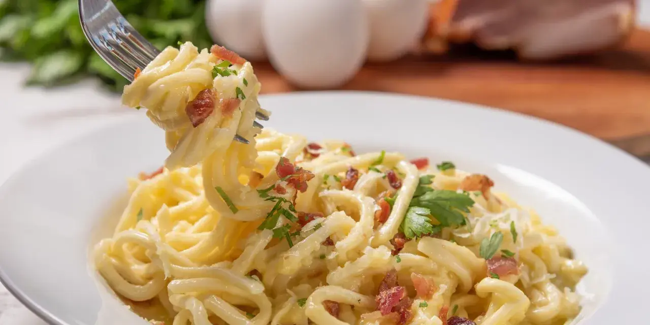 Pyszne spaghetti carbonara przepis na talerzu, z widocznymi jajkami i boczkiem w tle. Idealne danie dla miłośników włoskiej kuchni.