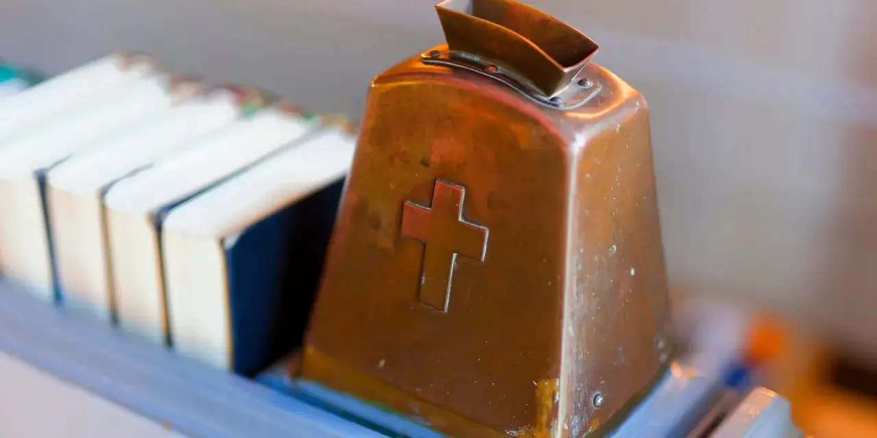 Kupferne Klingel mit Kreuz, bereit für Spenden. Hier wird über Kirchensteuer Befreiung nachgedacht.