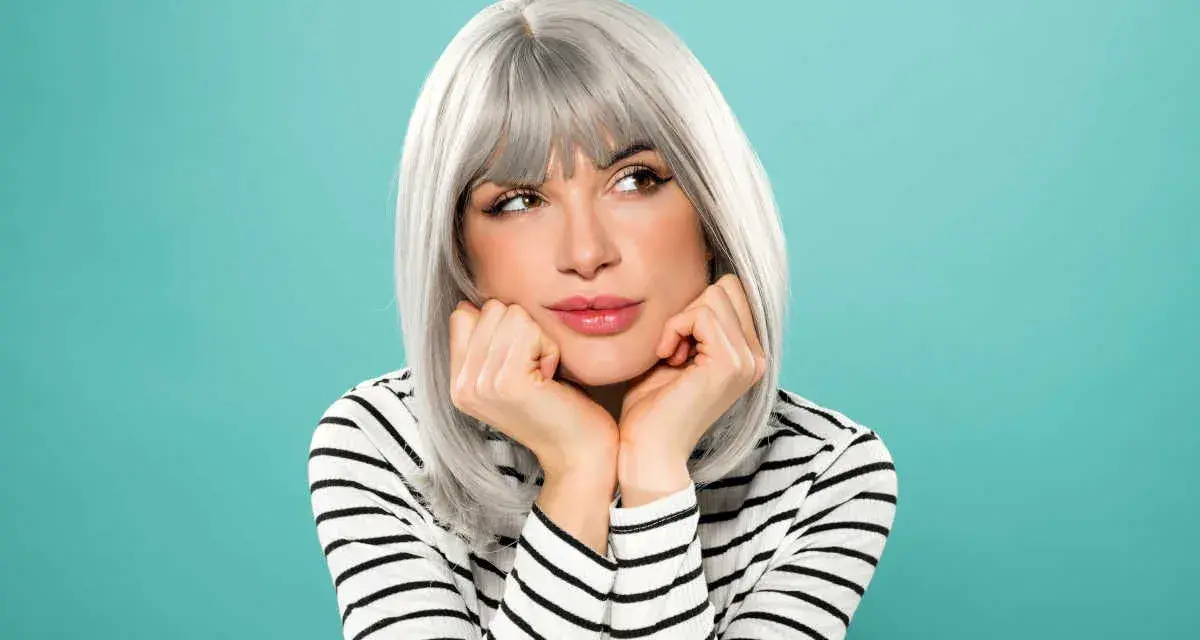 Donna con eleganti capelli grigi, appoggiata alle mani, con un'espressione sognante.