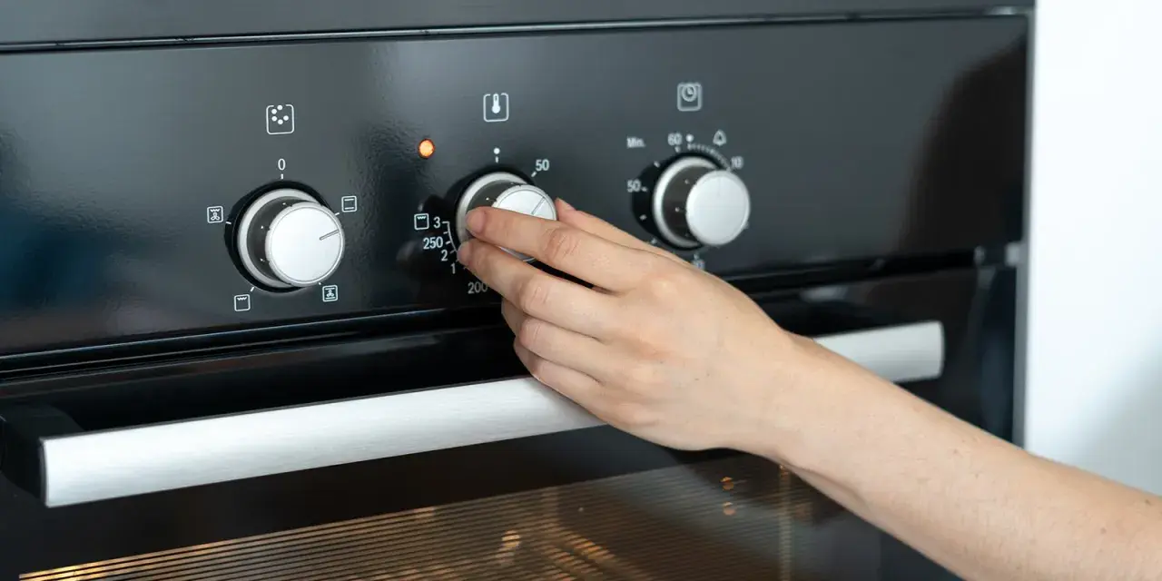 Hand dreht Temperaturregler am Ofen auf 250 Grad. Die Frage "wie lange Ofen vorheizen" wird durch das Einstellen der Temperatur beantwortet.