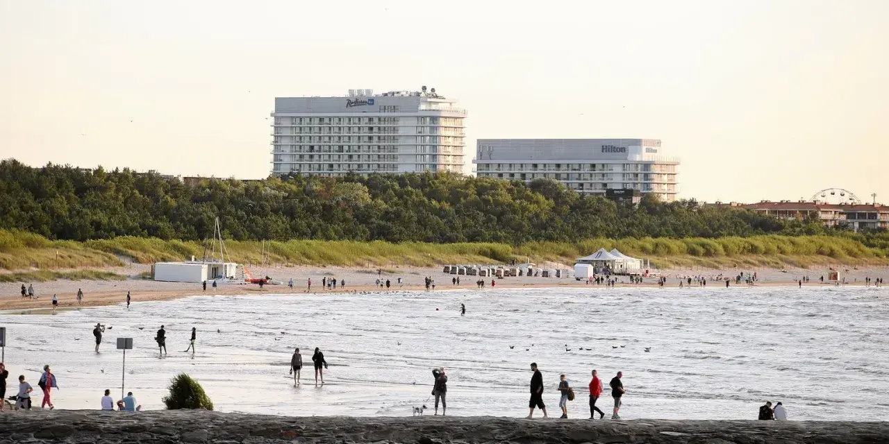 Ludzie spacerują po najszerszej plaży w Polsce, w tle hotele Radisson i Hilton.