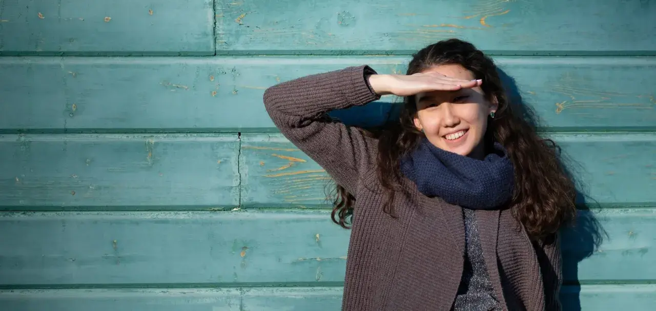 Ragazza sorride, coprendosi gli occhi dal sole. Il fastidio alla luce non le impedisce di godersi la giornata.