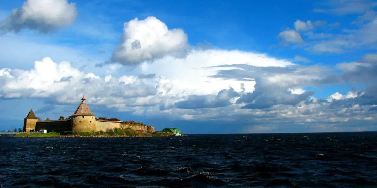 Forteca na wyspie nad największym jeziorem Europy, woda faluje pod błękitnym niebem z chmurami.