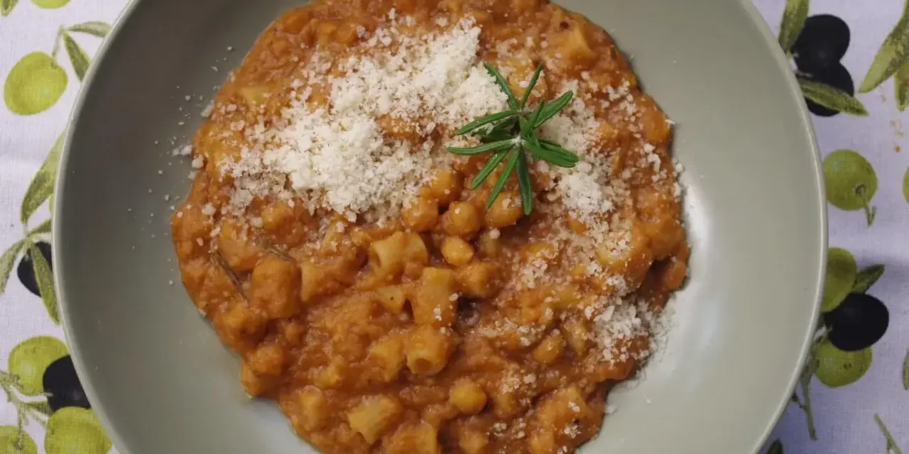 Pyszny makaron z ciecierzycy w sosie pomidorowym, posypany parmezanem i udekorowany gałązką rozmarynu.