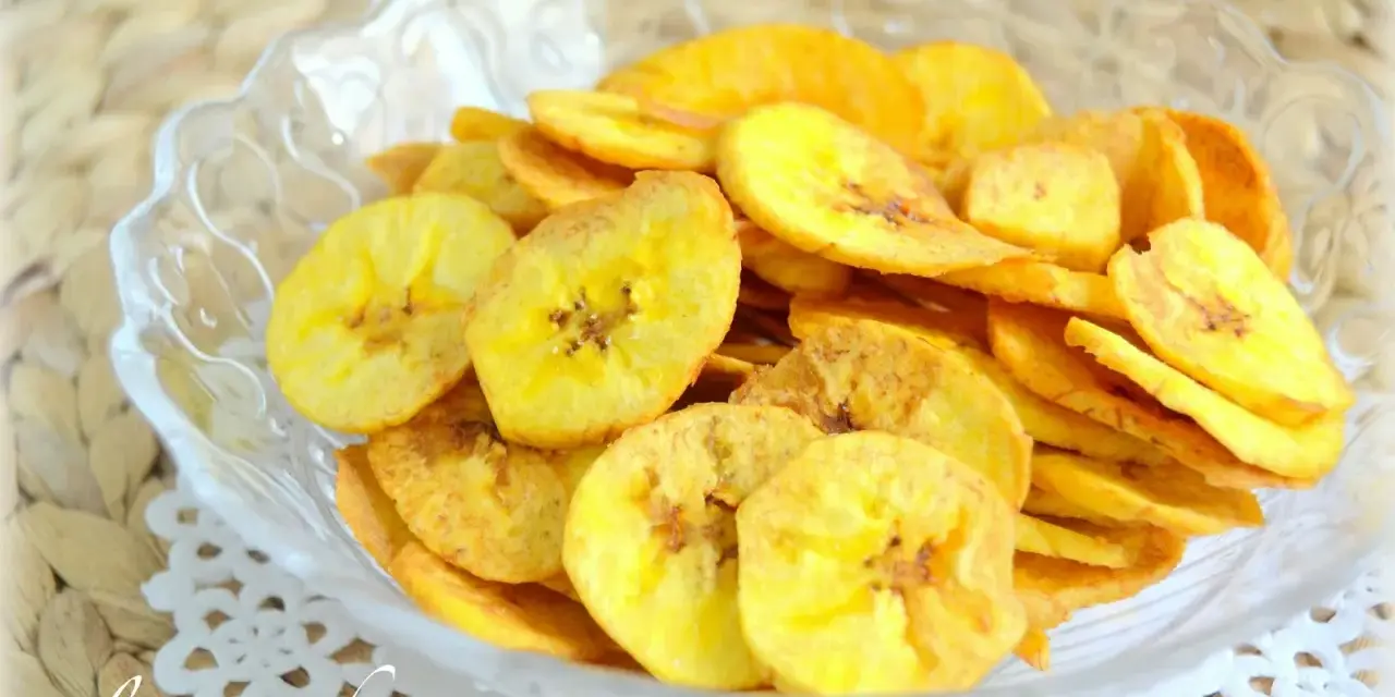 Crujientes rodajas de plátano frito doradas, servidas en un cuenco de cristal. Un delicioso snack casero.