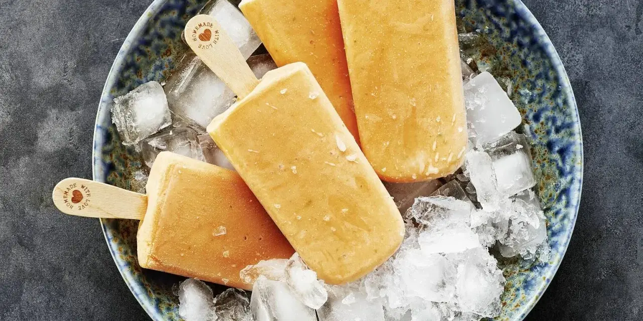 Vier selbstgemachte Papaya-Eis am Stiel liegen auf zerstoßenem Eis in einer blauen Schale.